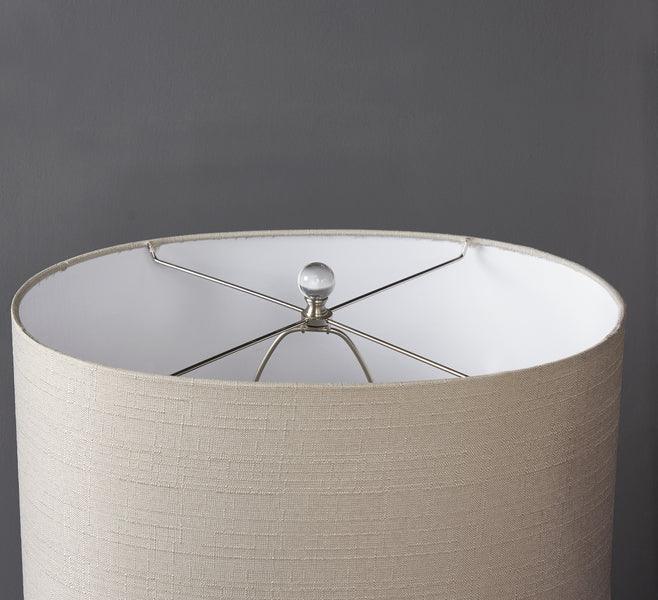Beige fabric drum lampshade with white lining and chrome finial against grey wall