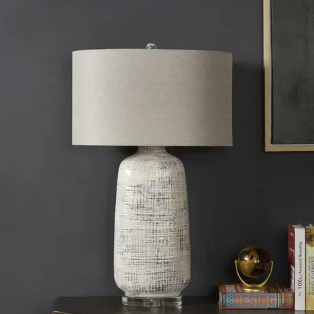 Ceramic table lamp with textured white base and beige fabric shade on sideboard