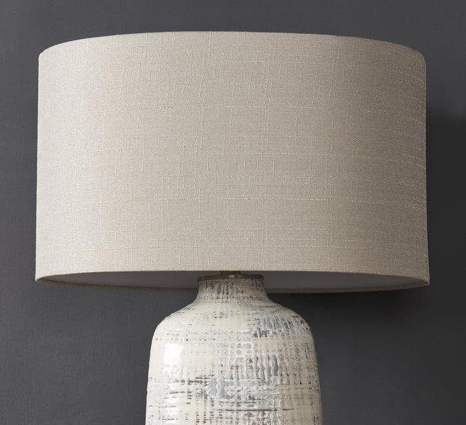 Ceramic table lamp with textured base and large beige fabric lampshade against dark wall