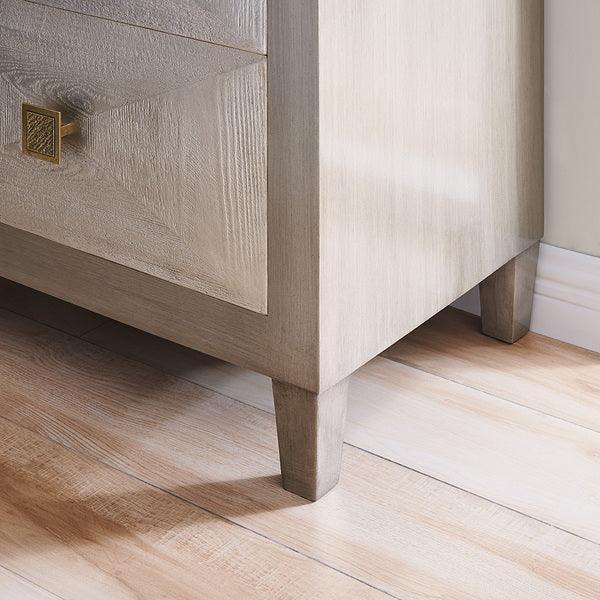 Light oak bedside table corner with geometric drawer front and gold handle on wood flooring