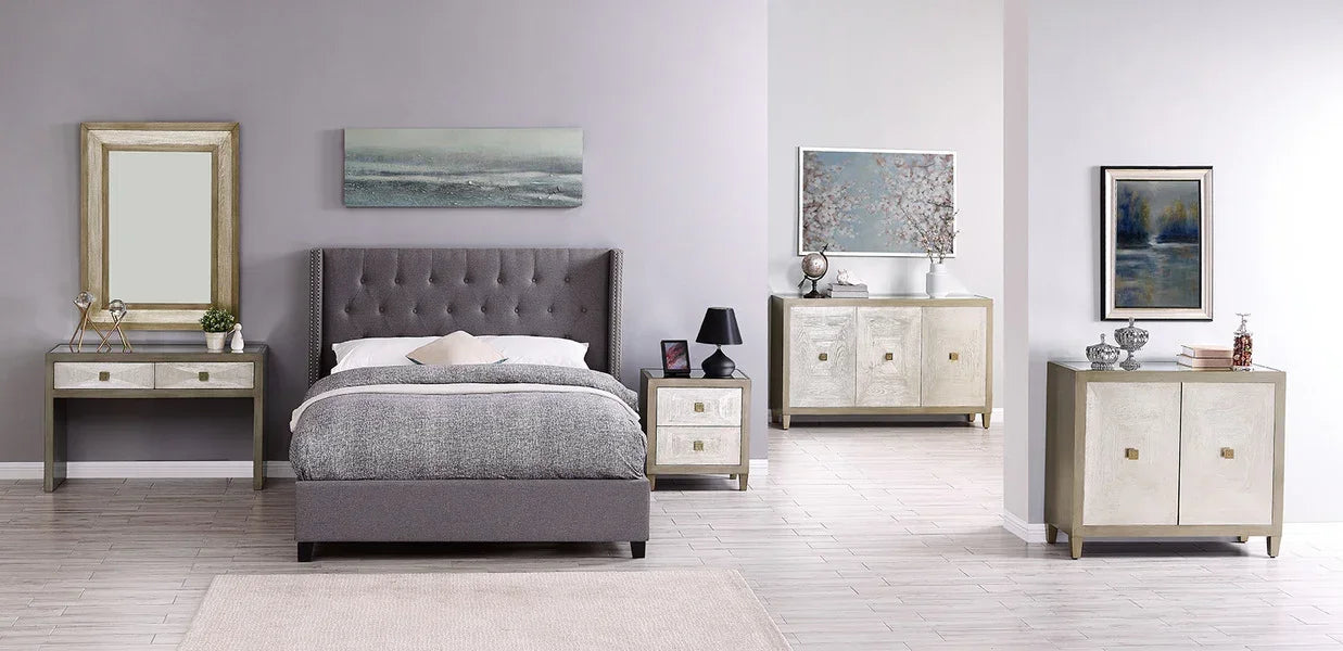 Grey upholstered bed with buttoned headboard, matching nightstand, and mirrored furniture