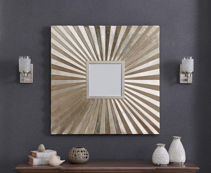 Square sunburst wall mirror with metallic gold frame mounted on dark grey wall