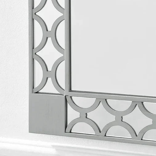 Silver geometric mirror frame with decorative cut-out pattern against a white wall