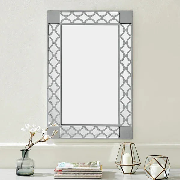 Rectangular wall mirror with geometric frame above shelf with candles, vase, and magazines