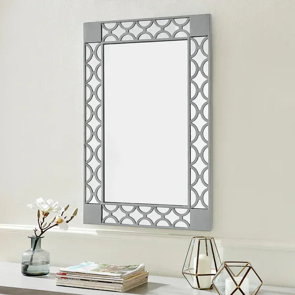 Rectangular wall mirror with geometric silver frame above console table with vase and decor
