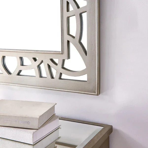 Silver geometric wall mirror above glass top console table with stacked books