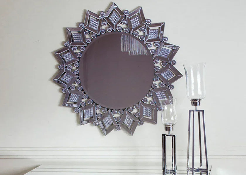 Round decorative wall mirror with geometric silver frame above modern glass candle holders