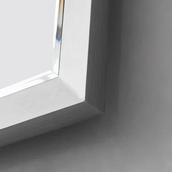 Closeup of rectangular silver mirror frame with beveled glass against grey wall