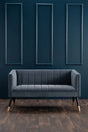 Dark grey velvet sofa with gold-tipped legs against blue paneled wall and wood floor