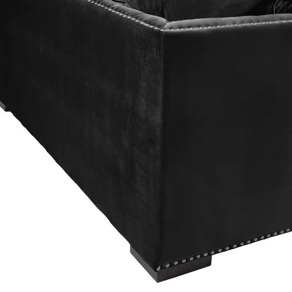 Black velvet sofa corner with studded trim and low wooden foot