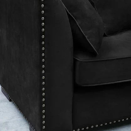 Black velvet sofa arm with silver stud detailing and scatter cushions on blue rug