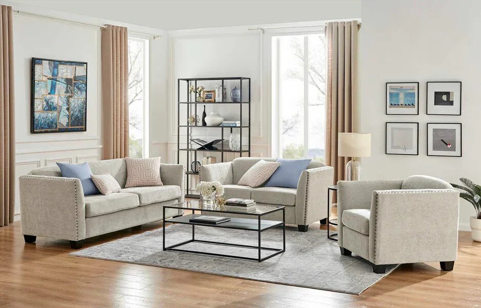 Light grey sofa set with studded arms, glass coffee table, and pastel cushions in bright living room