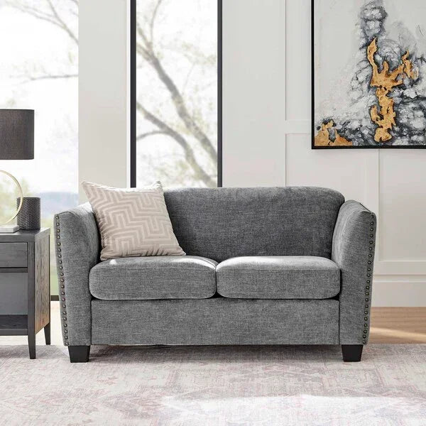 Grey fabric sofa with studded arms and patterned cushion in a modern living room