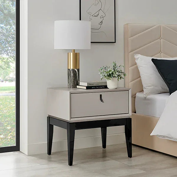 Modern bedside table with drawer, marble lamp, books, and plant next to upholstered bed