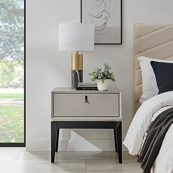 Modern bedside table with drawer, marble lamp, and plant next to upholstered bed