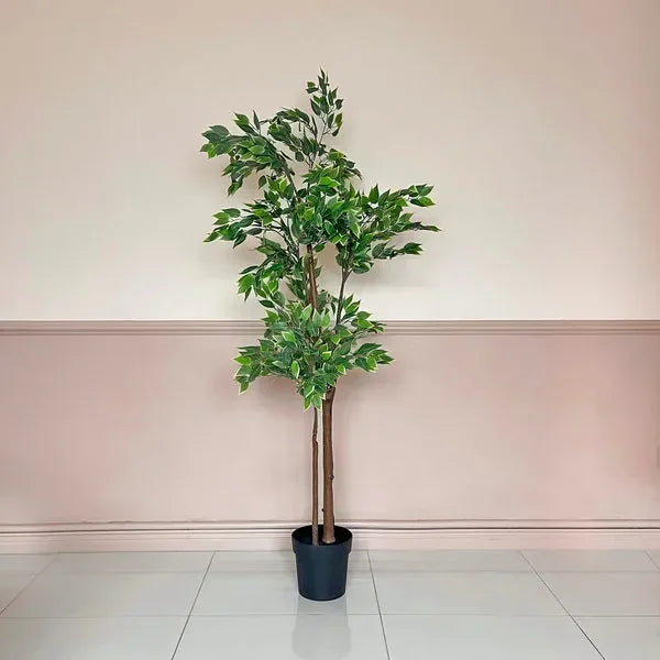 Artificial potted plant with green leaves on white tile floor against pale pink wall
