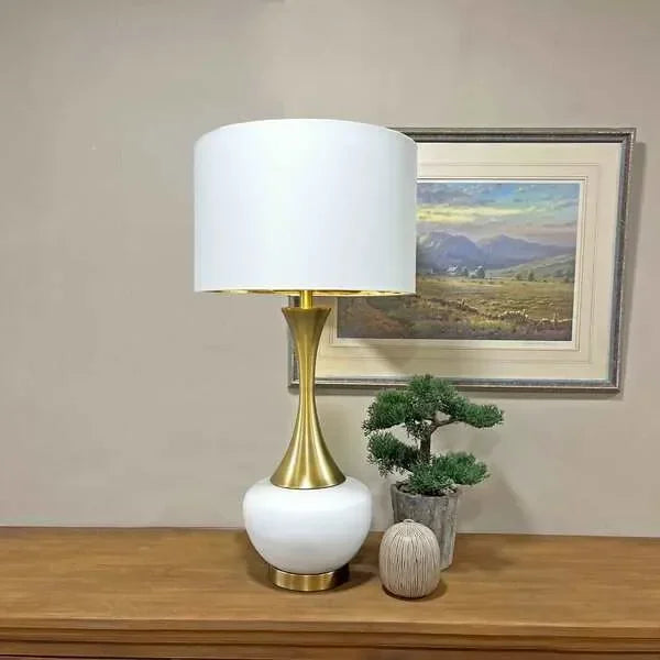 Modern table lamp with gold and white base beside potted plant on wooden sideboard