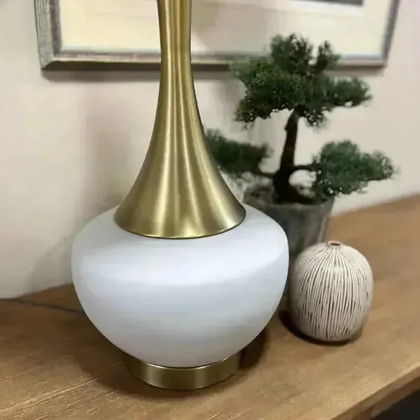 Gold and white table lamp on wooden sideboard with potted plant and decorative ornament