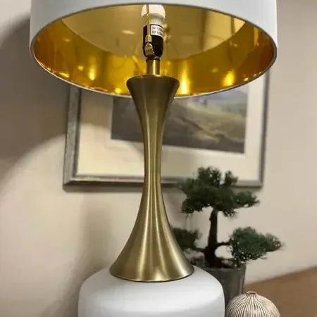 Modern table lamp with gold stem and white base on wooden sideboard