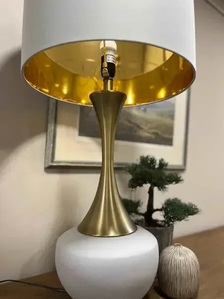 Modern table lamp with gold stem and white base on wooden sideboard