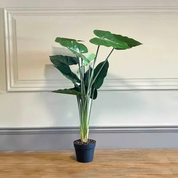 Artificial potted plant with large green leaves on wooden surface against cream wall
