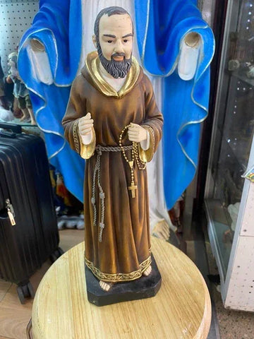 Brown religious figurine in monk robe holding rosary, displayed on round wooden table