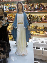Religious figurine of a woman in white and blue robes displayed among assorted statues