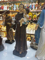 Brown religious figurine holding child and lilies, displayed among assorted church statues