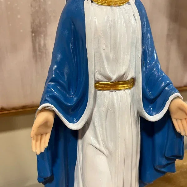 Religious figurine in white robe with blue cloak, gold belt, hands open on table