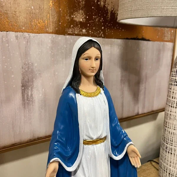 Religious figurine with blue and white robe on wooden table near abstract artwork