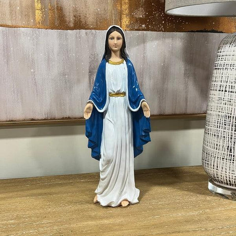 Religious statue with blue and white robe on wooden table beside patterned lamp