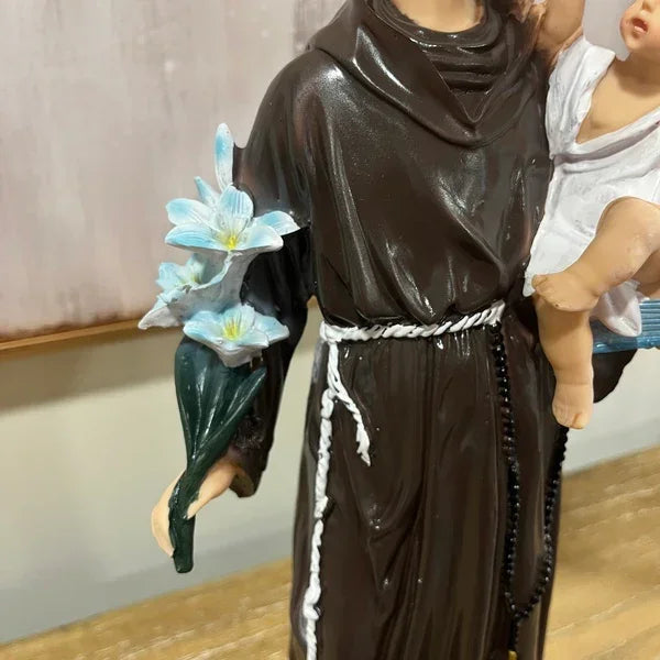 Brown robed religious statue holding blue lilies and child, displayed on wooden surface