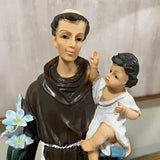 Religious figurine of saint in brown robe holding child and blue lilies