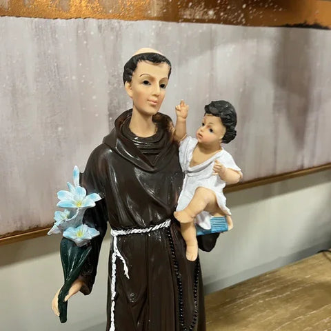 Religious figurine featuring saint in brown robe holding flowers and child on indoor table