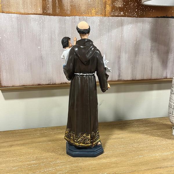 Brown religious statue with gold trim on wooden table, figure holding child and lily flower