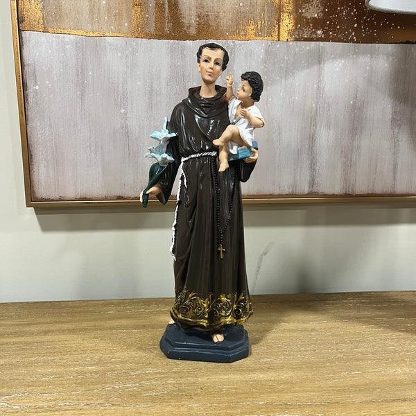 Brown robed saint figurine holding child, standing on wooden table, wall art behind