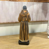 Brown robed monk figurine on wooden table with decorative trim, rear view