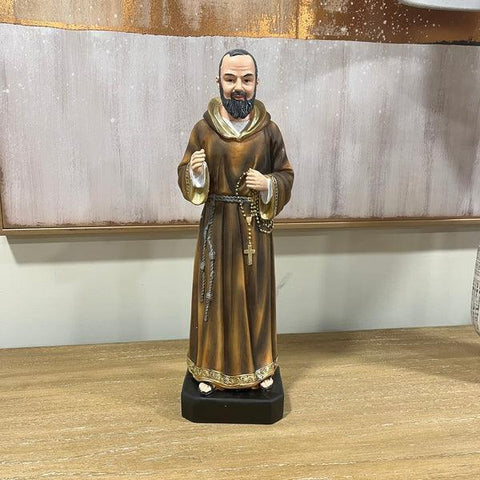 Brown robed religious figurine with rosary on wooden table against neutral wall art