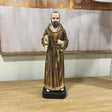 Brown robed religious figurine with rosary on wooden table against neutral wall art