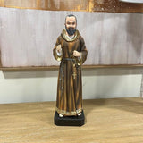 Brown robed religious figurine with rosary on wooden table against neutral wall art