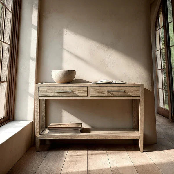 Light oak console table with two drawers, lower shelf, bowl and books by a sunlit window