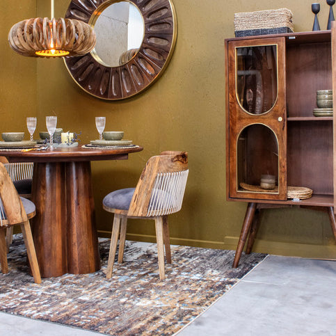 Wooden dining table and chairs with glass cabinet and round mirror in dining room