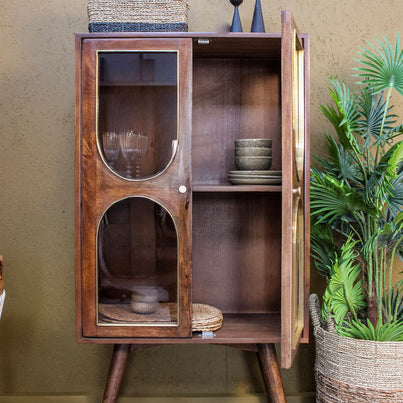 Wooden cabinet with glass doors and mid-century style legs, decorated with bowls and basket