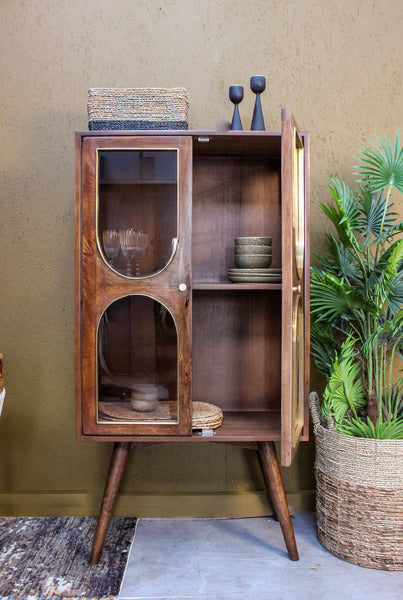 Wooden cabinet with glass doors and mid-century style legs, decorated with bowls and basket