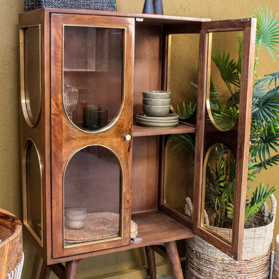 Brown wooden cabinet with glass doors, decorative bowls inside, basket on top