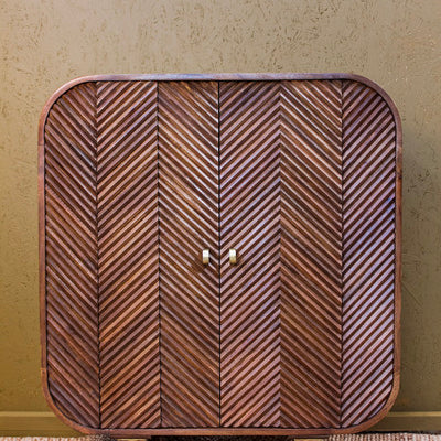 Wooden cabinet with layered chevron pattern doors and rounded edges on brass legs