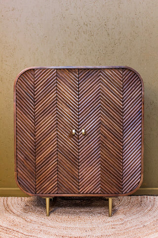 Wooden cabinet with layered chevron pattern doors and rounded edges on brass legs