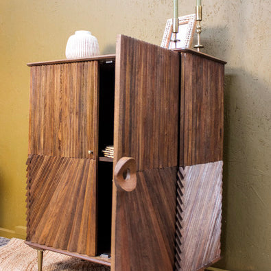 Wooden cabinet with diagonal chip design and brass legs on woven rug