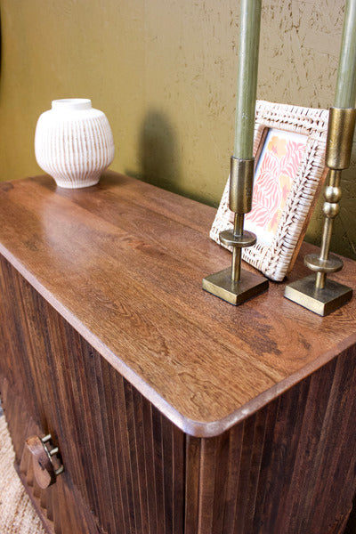 Wooden cabinet top with decorative white vase, photo frame and brass candle holders