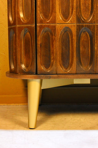 Close-up of wooden sideboard with oval tile carvings and gold tapered leg